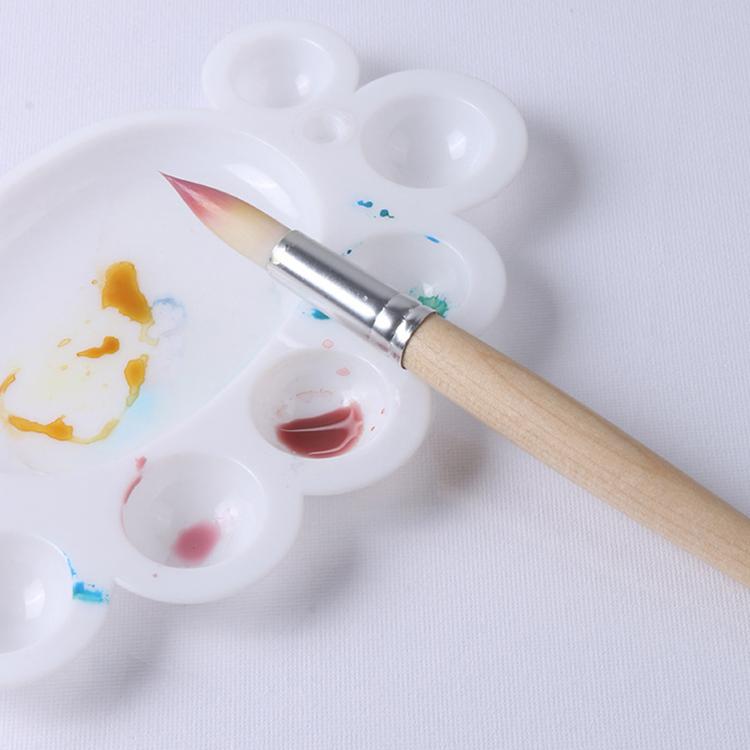 Small paintbrush with silver ferrule on white paint palette with mixed colors