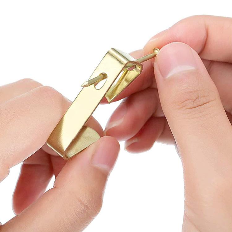 Gold picture hanging hook with nail, shown held in hands