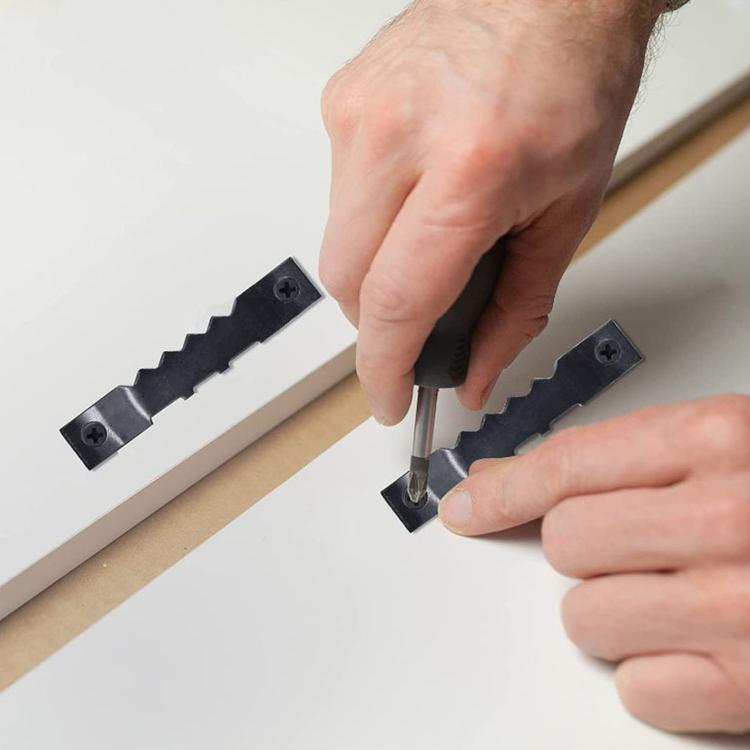 Hands installing black sawtooth picture hooks with screws on a frame edge