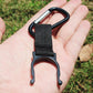 Black strap bottle holder clip with rounded metal hook, shown in palm