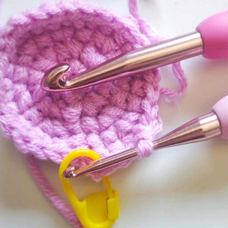 Crochet hook in use with pink yarn and stitch holder, showing metal hook head