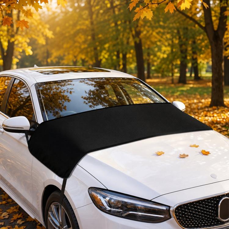 Front windshield cover in black fabric on a car hood, with scattered leaves visible