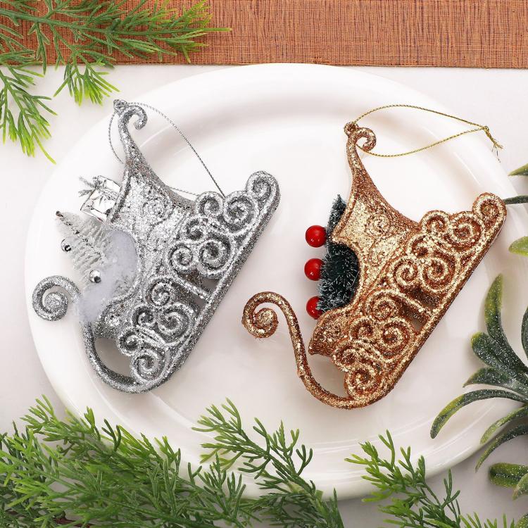 Two glitter sleigh ornaments on a plate: silver with beads and gold with pine accents