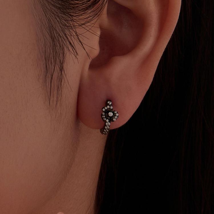 Zircon-studded cross-motif hoop earrings on a person’s ear, black-tone finish