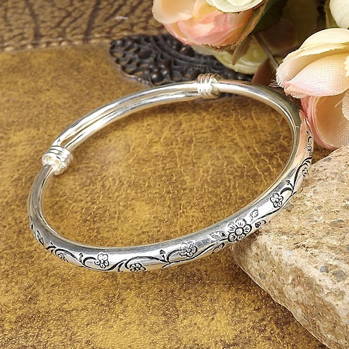 Silver oval cuff bracelet with engraved floral scrolls and raised knot ends