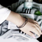Black multi-layer open cuff charm bracelet worn on wrist with angular links.