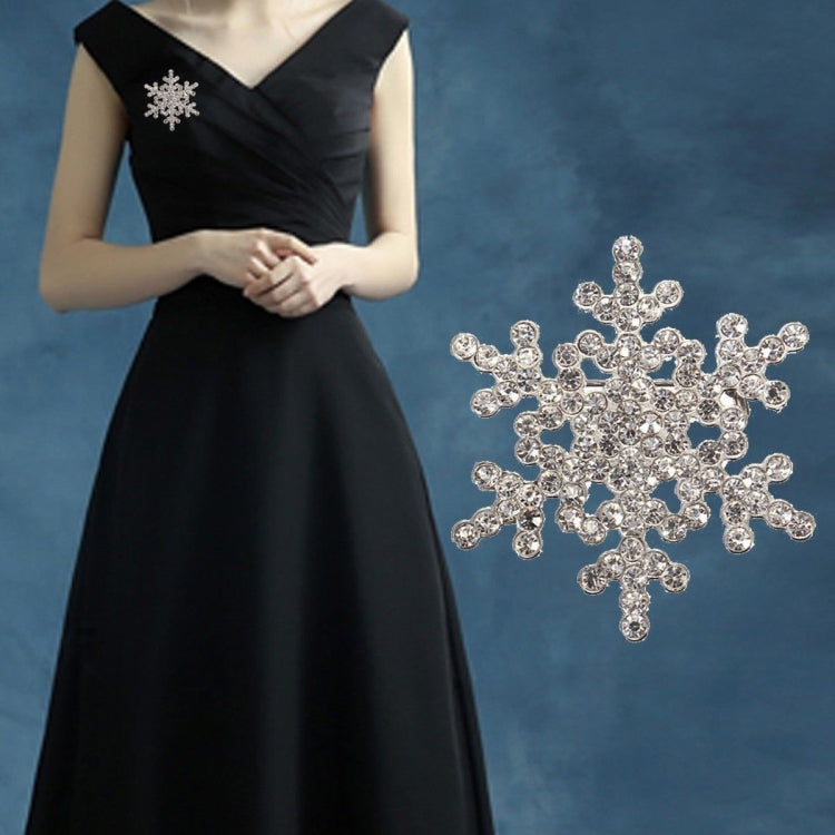Silver-tone rhinestone snowflake brooch with dangling pin, worn on dark dress