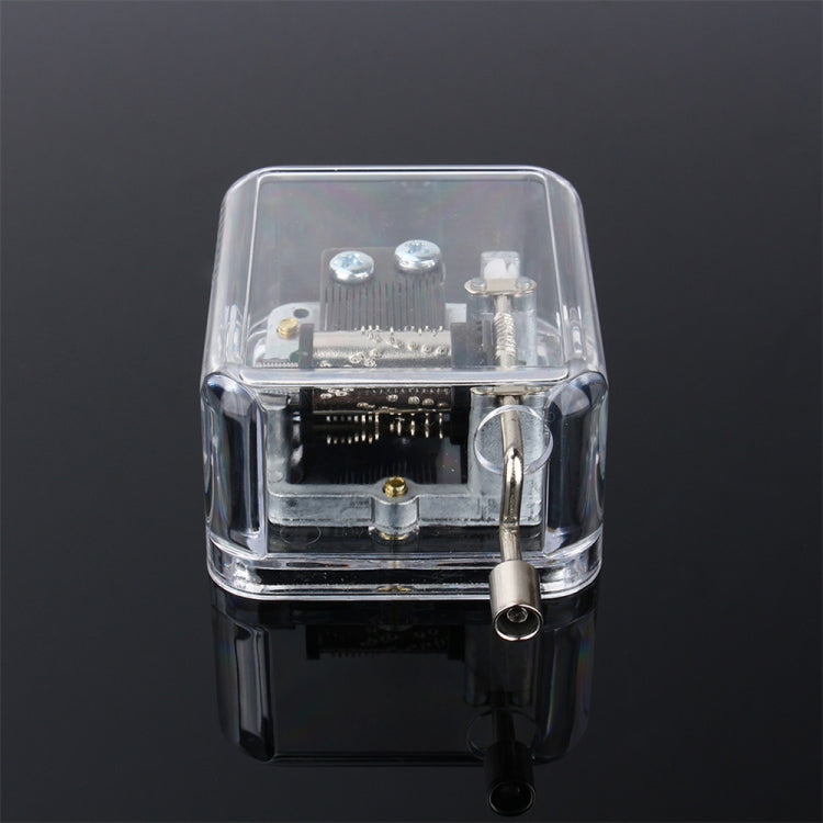 Clear acrylic DIY music box with exposed mechanism and crank spindle, front view