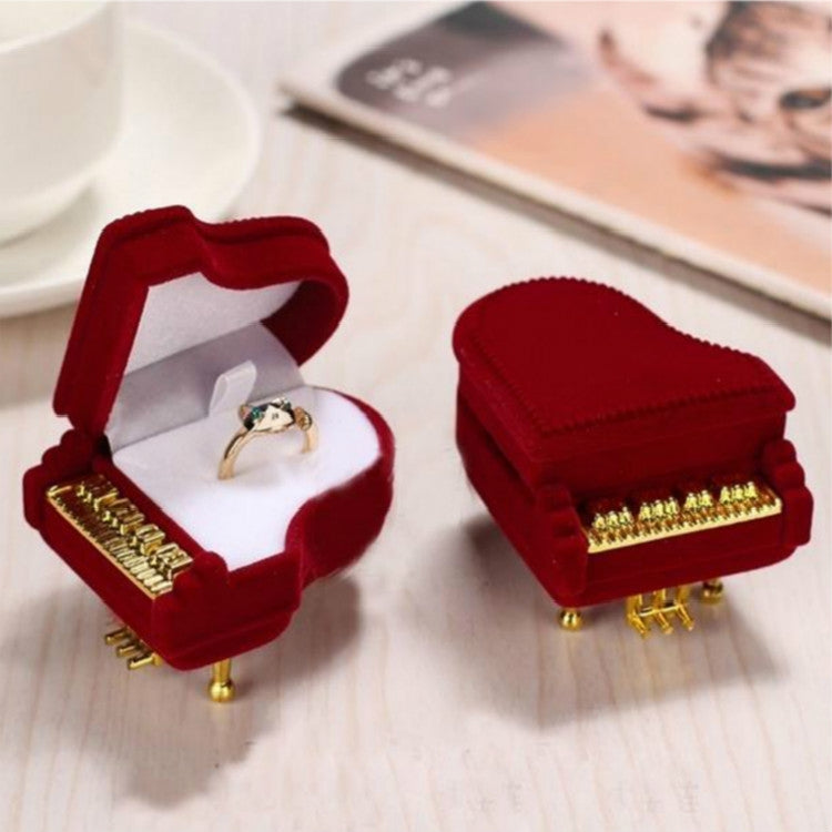 Red velvet piano-shaped jewelry box with lid open, ring displayed on white cushion