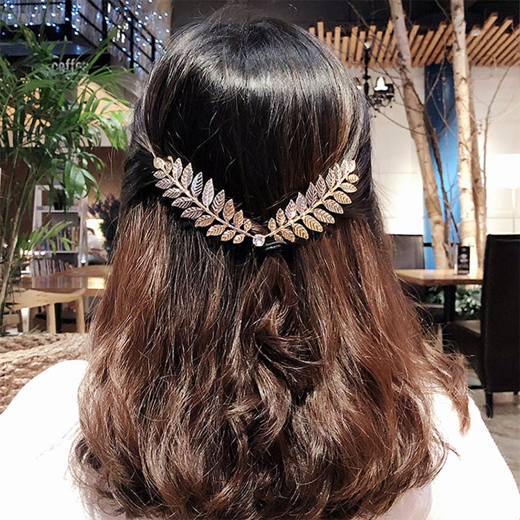 Gold leaf hair headband worn on dark wavy hair, with rhinestone centerpiece