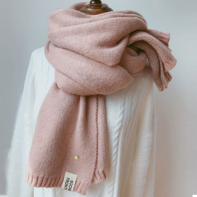 Pink thick knit scarf draped with ribbed ends and small woven brand label