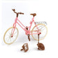 Mini dollhouse bicycle with pink frame and tan wheels, plus loose brown front parts