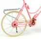 Close-up mini dollhouse bicycle: pink fork, tan wheel rims, gray front guard