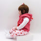 Baby girl silicone doll lying on a block, wearing a pink hooded vest and white patterned pajamas
