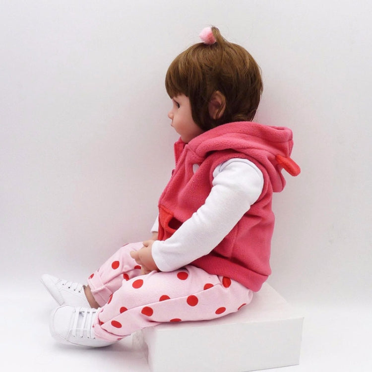 Baby girl silicone doll lying on a block, wearing a pink hooded vest and white patterned pajamas