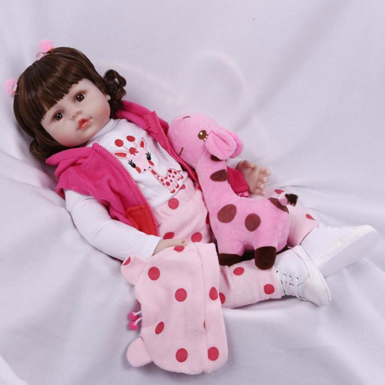 Baby girl silicone doll reclining with pink hooded outfit, white patterned pants, and plush pink toy