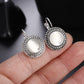 Close-up of round drop earrings with white cabochon and ornate silver filigree borders
