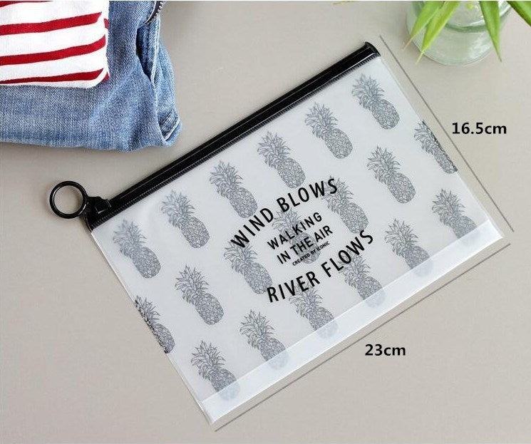 Transparent PVC cosmetic bag with gray pineapple print, black zipper, wrist loop, flat lay