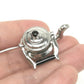 Miniature metal tea kettle with black knob lid, silver spout and side handles in hand.