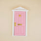 Miniature fairy tale door, pink with gold handle and latch, white frame