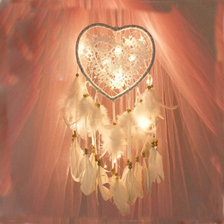 Heart dream catcher hanging with white feathers and warm fairy lights along the web