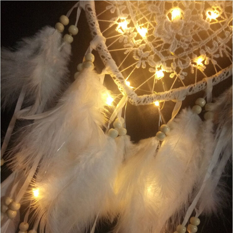 Close-up of heart dream catcher with white feathers and warm fairy lights