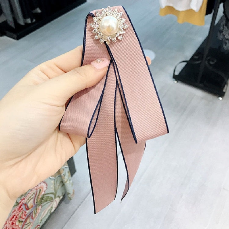 Pink satin bow-knot brooch held in hand, rhinestone faux pearl centerpiece and long tails