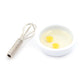 Miniature manual egg beater with coiled spring handle and small bowl of two eggs