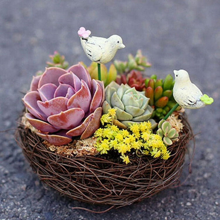 Woven rattan bird nest with two white bird figures and succulent plants