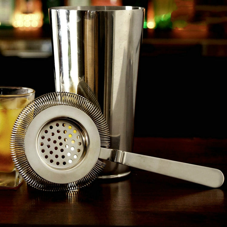 Stainless steel ice trap strainer with perforated disc and long handle, shown on bar setup