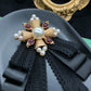 Black lace bow brooch with pearl center, gold spikes, and dark red gem accents