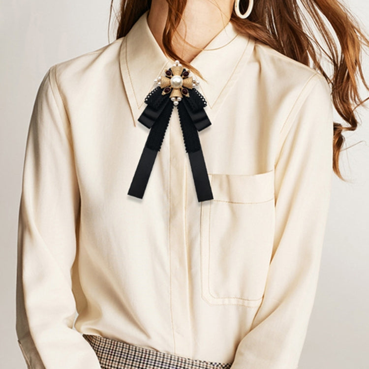 Black lace ribbon bow pin with pearl center worn on a light cream shirt neckline