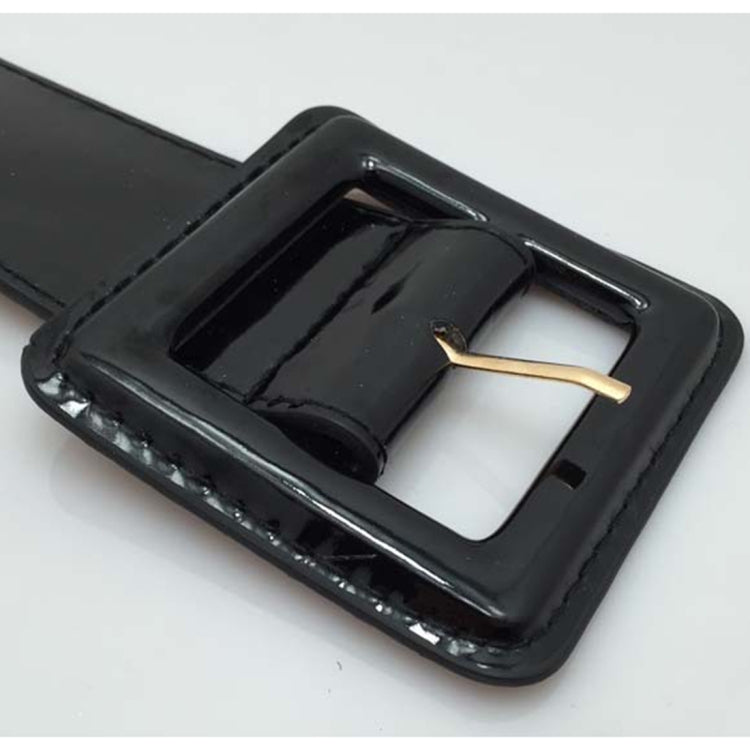 Close-up of square black glossy buckle on wide belt with gold-tone bar