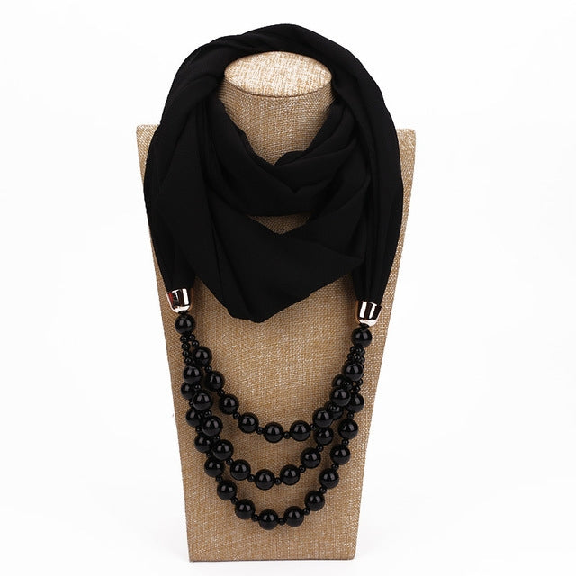 Black scarf with imitation pearl bead necklace, draped with layered dark beads.
