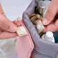 Hands inserting toiletries into a pink wash bag with gray lining and mesh sleeves