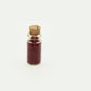 Mini glass food bottle with cork, clear body filled with dark red granules