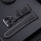 Black leather watch band with perforated holes, yellow stitching, and metal buckle.