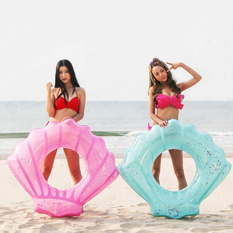 Two shell-shaped inflatable swimming rings in pink and light blue on beach sand