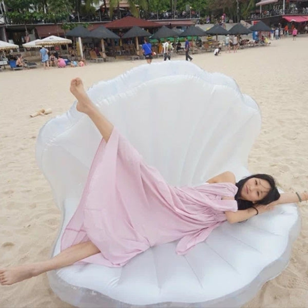 White scallop-shaped inflatable swimming floating mat on sandy beach