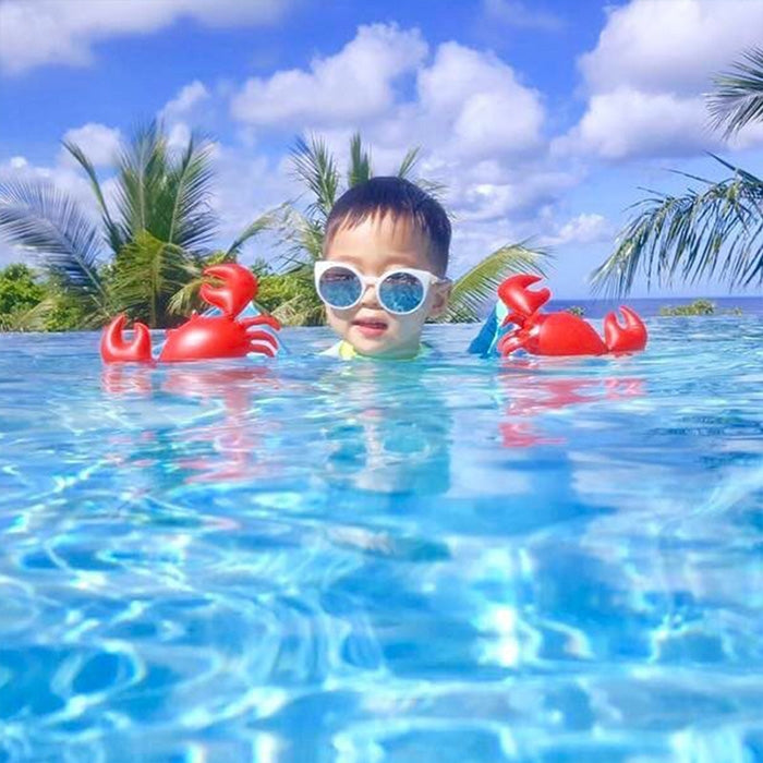 Child swimming wearing red crab-shaped inflatable arm floats and blue swim goggles