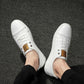 Men's white lace-up sneakers, top view with eyelets, laces, and tan brand label