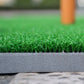 Close-up of green turf and gray backing edge on a golf practice mat